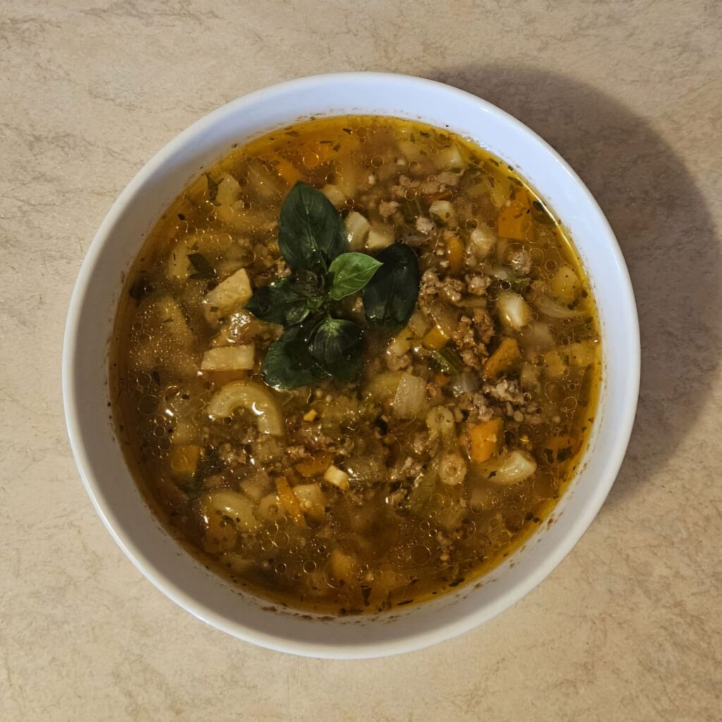 Deep bowl of Beef Macaroni Vegetable Soup served and garnished with fresh basil.