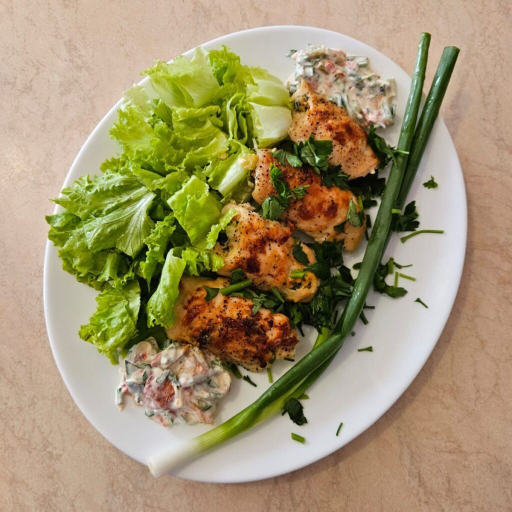 Serving plate with stuffed mini rolled chicken bites, fresh arugula, whole spring onion, leftover filling, and chopped parsley garnish.
