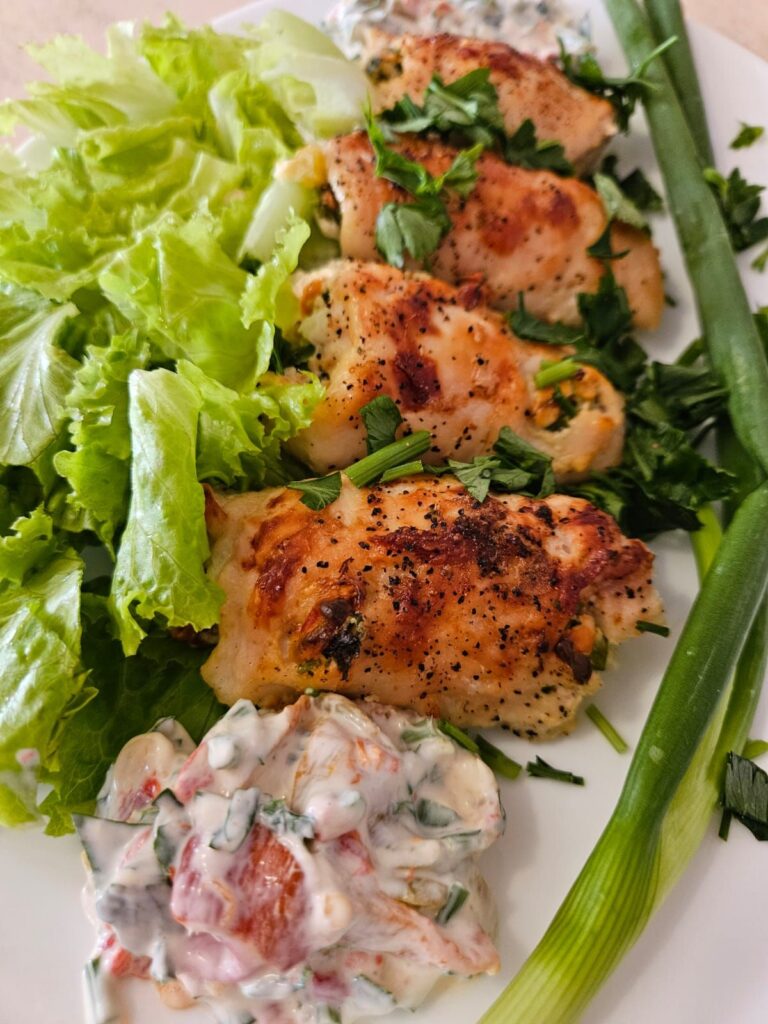 Close-up of a serving plate with four mini rolled chicken bites, fresh arugula, whole spring onion, extra creamy filling, and parsley garnish.