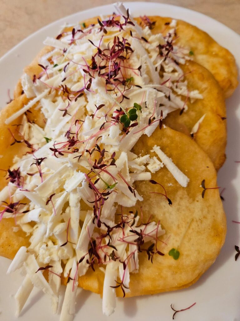 Three mekici served with grated cheese, honey, and microgreens in a plate.