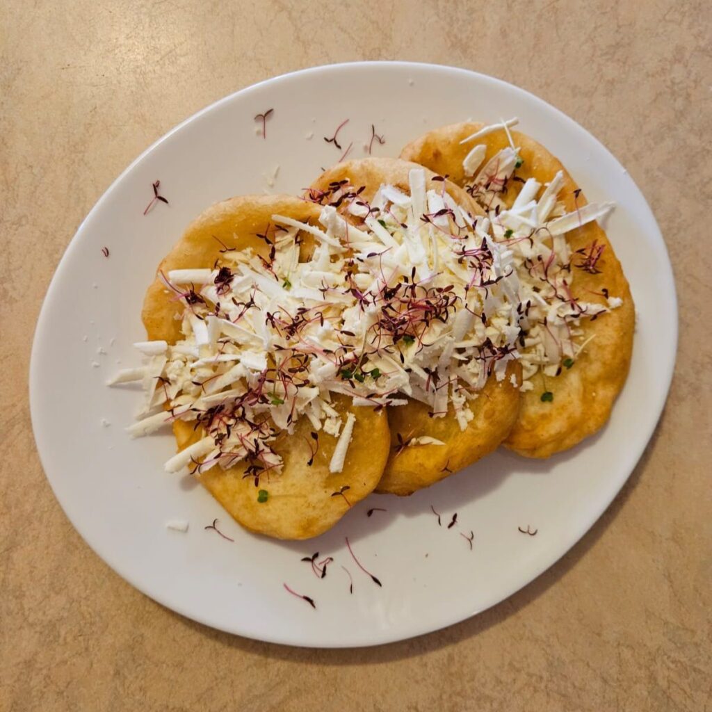 Plate of mekica topped with grated cheese, honey, and microgreens photographed from above.