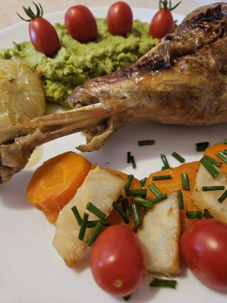 Close-up of tender turkey drumsticks with pea mash and roasted vegetables on a plate.