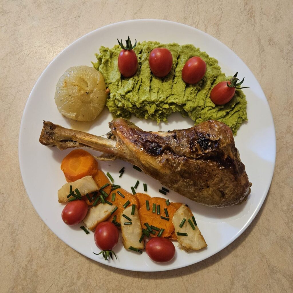 Tender Turkey Drumsticks Recipe served with pea mash, roasted vegetables, cherry tomatoes, and fresh chives on a plate.