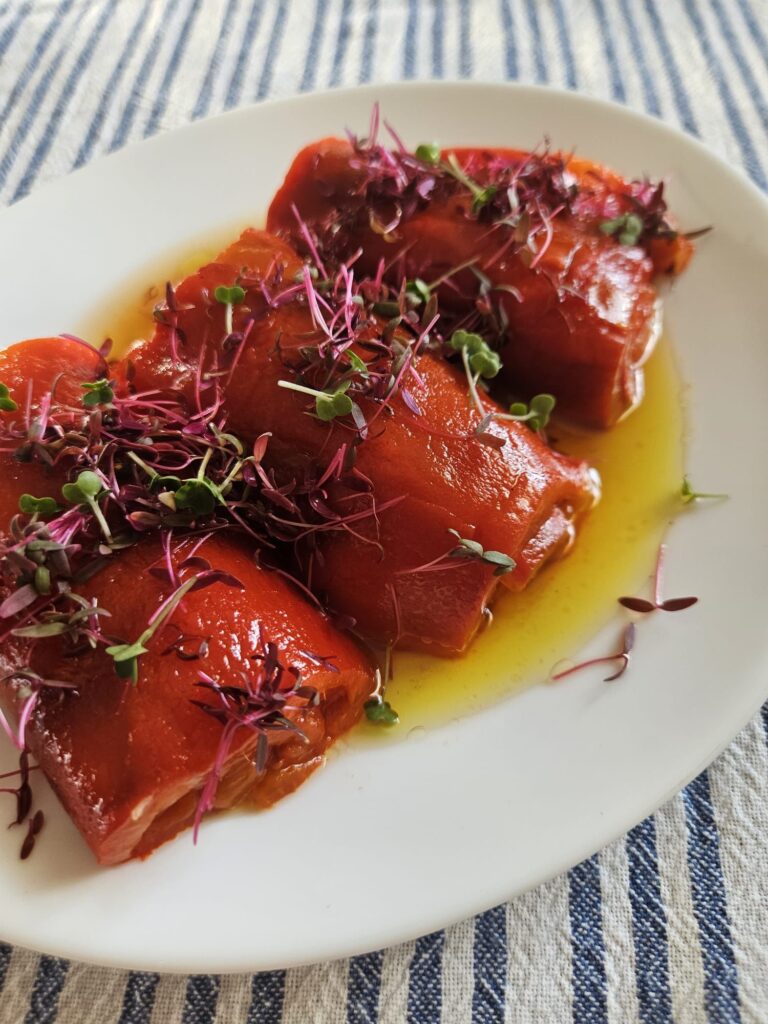 Close side view of rolled roasted peppers with microgreens on a plate.