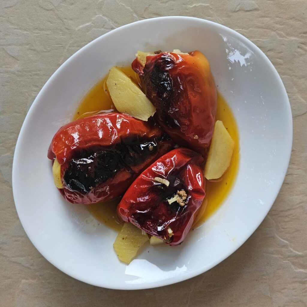 Three baked rice pork filled peppers served on a plate with a potato slice.