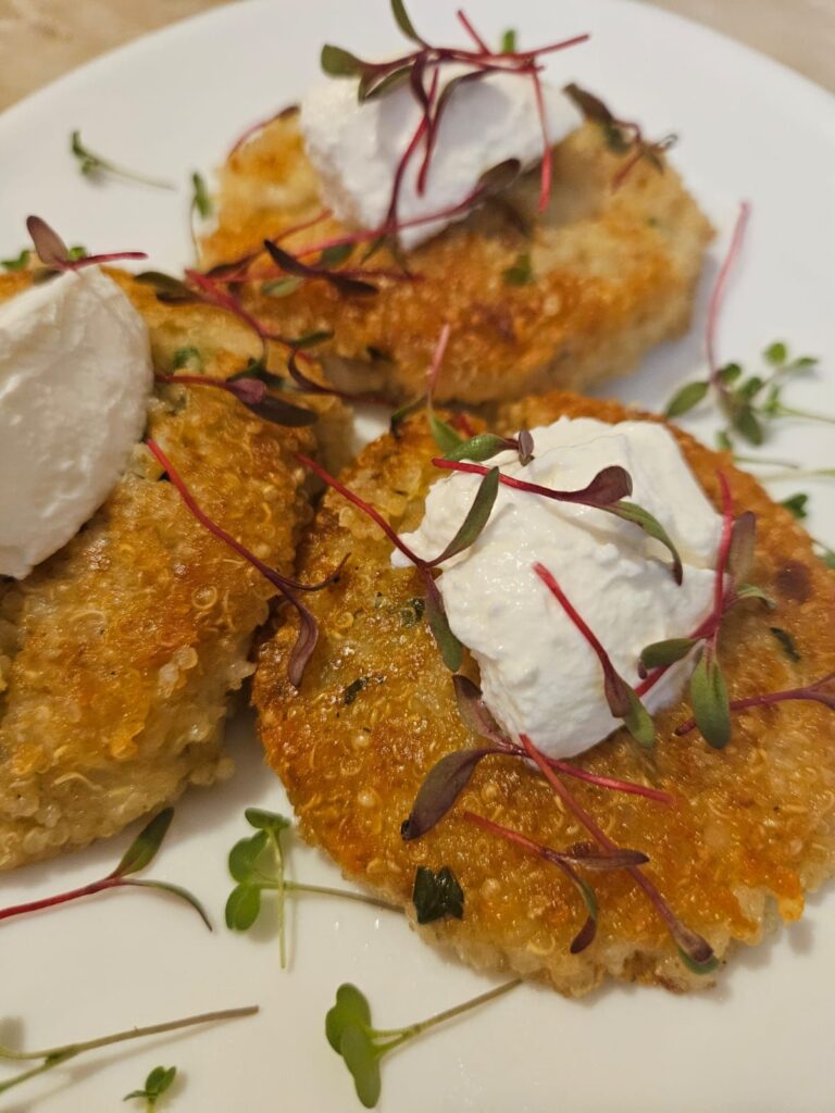 Three quinoa cakes with cream cheese and microgreens served on a plate close up.