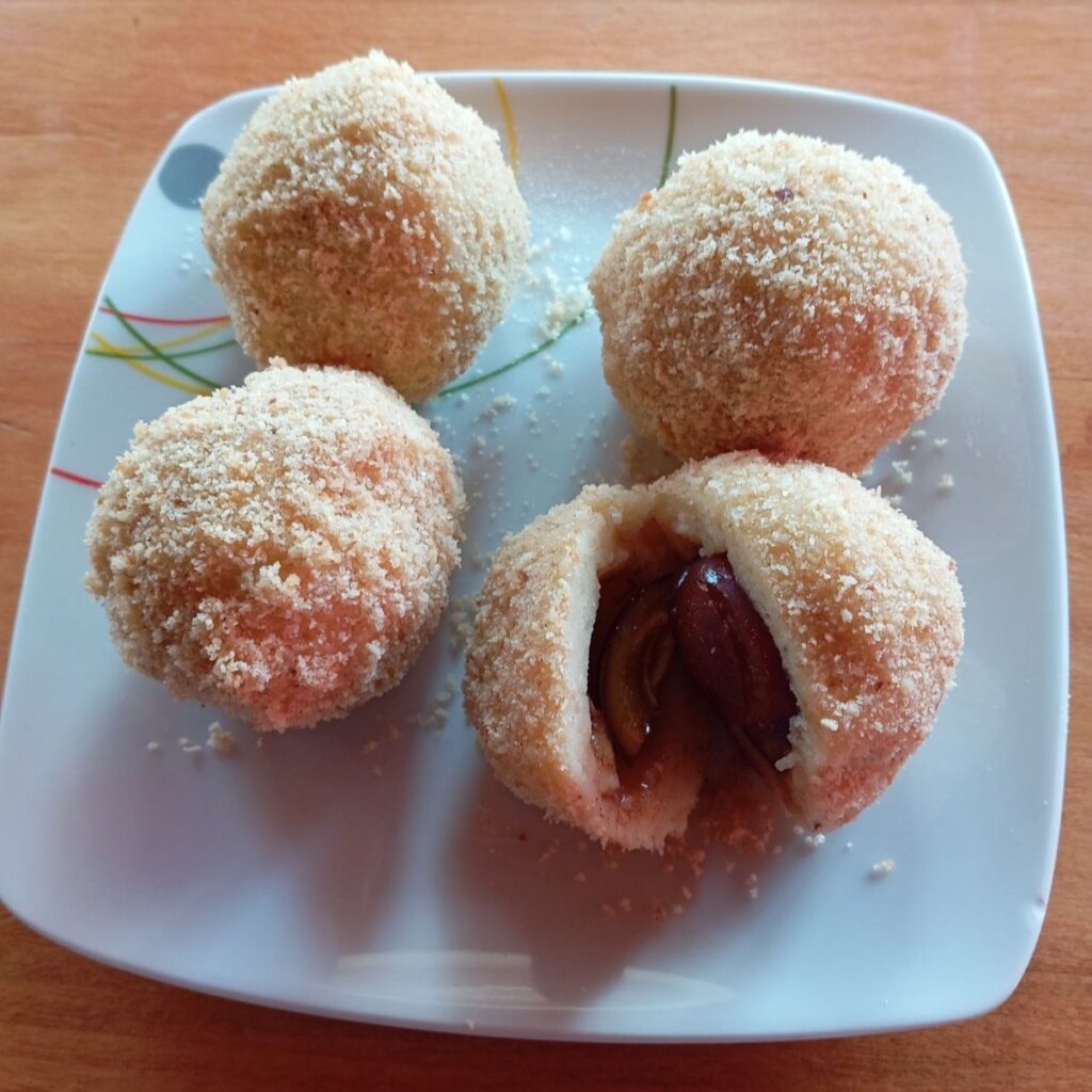 Four potato plum sweet dumplings served on a plate, with one cut in half to show the juicy filling inside.