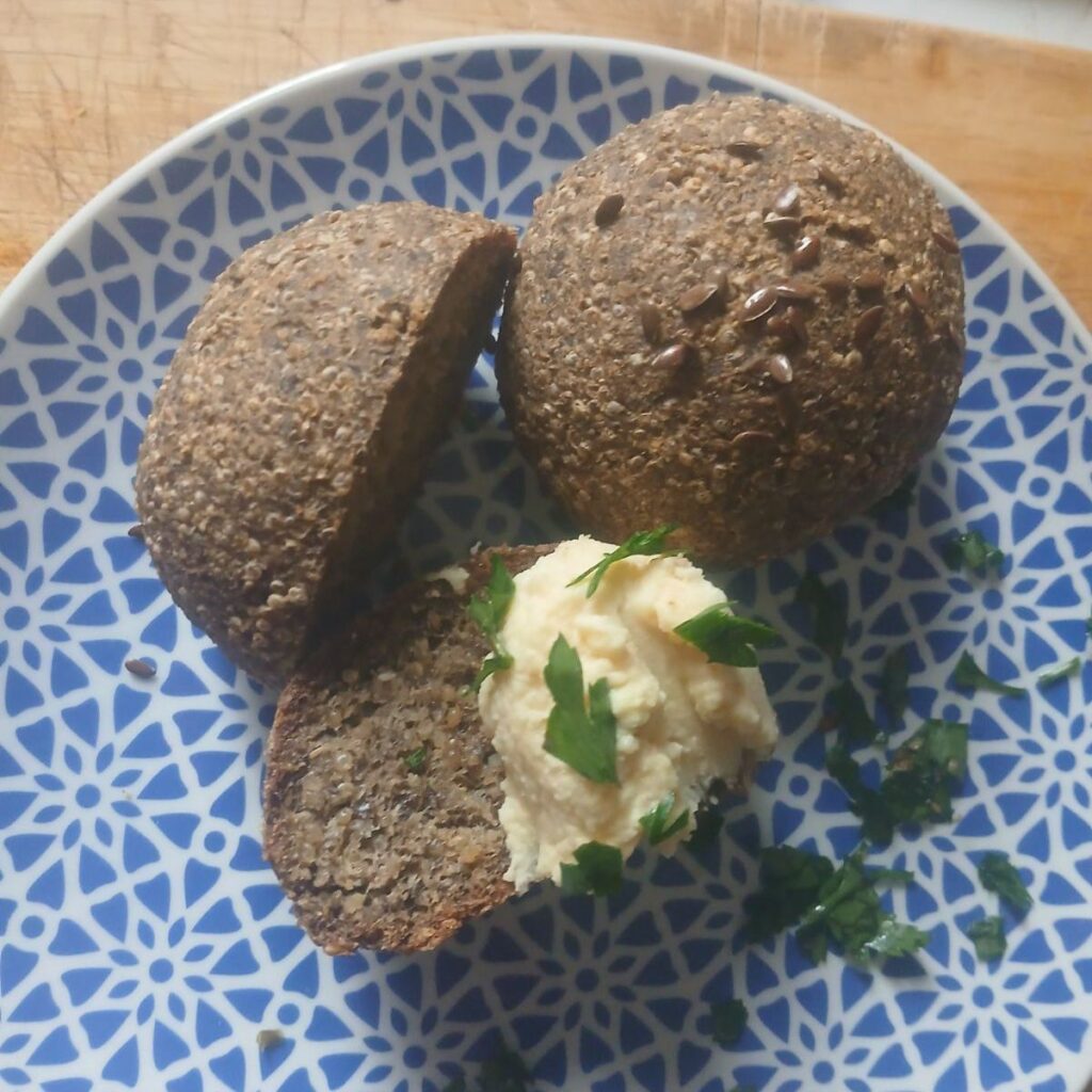 Mini Quinoa Breads with Chia served on a plate, one whole, one half, and one slice with chickpea spread and parsley.