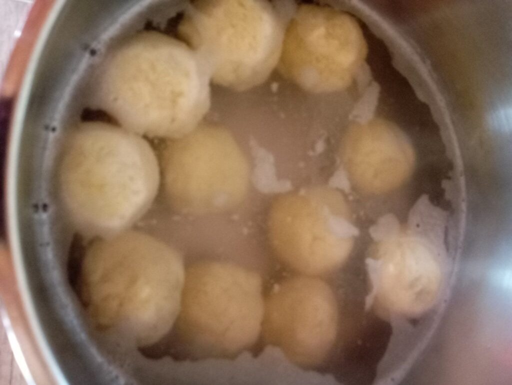 Potato plum dumplings cooking in a large pot of gently boiling water.