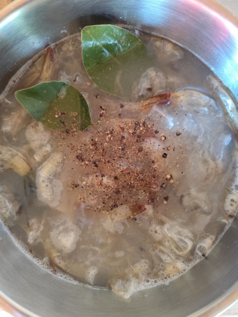 Shrimp shells in a pot with bay leaves, salt, and pepper covered with water.