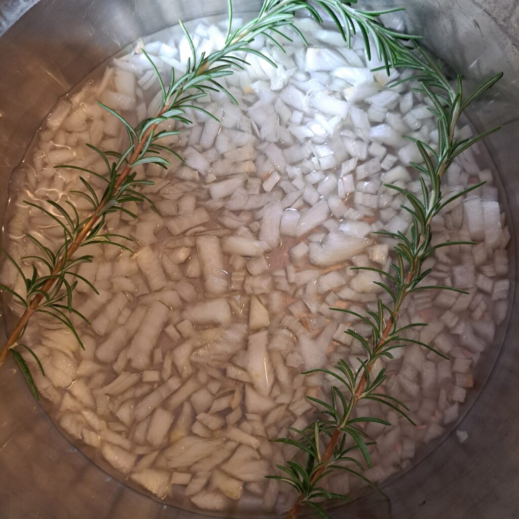 Chopped onion, water, and rosemary sprigs in a deep pot ready for ribs.