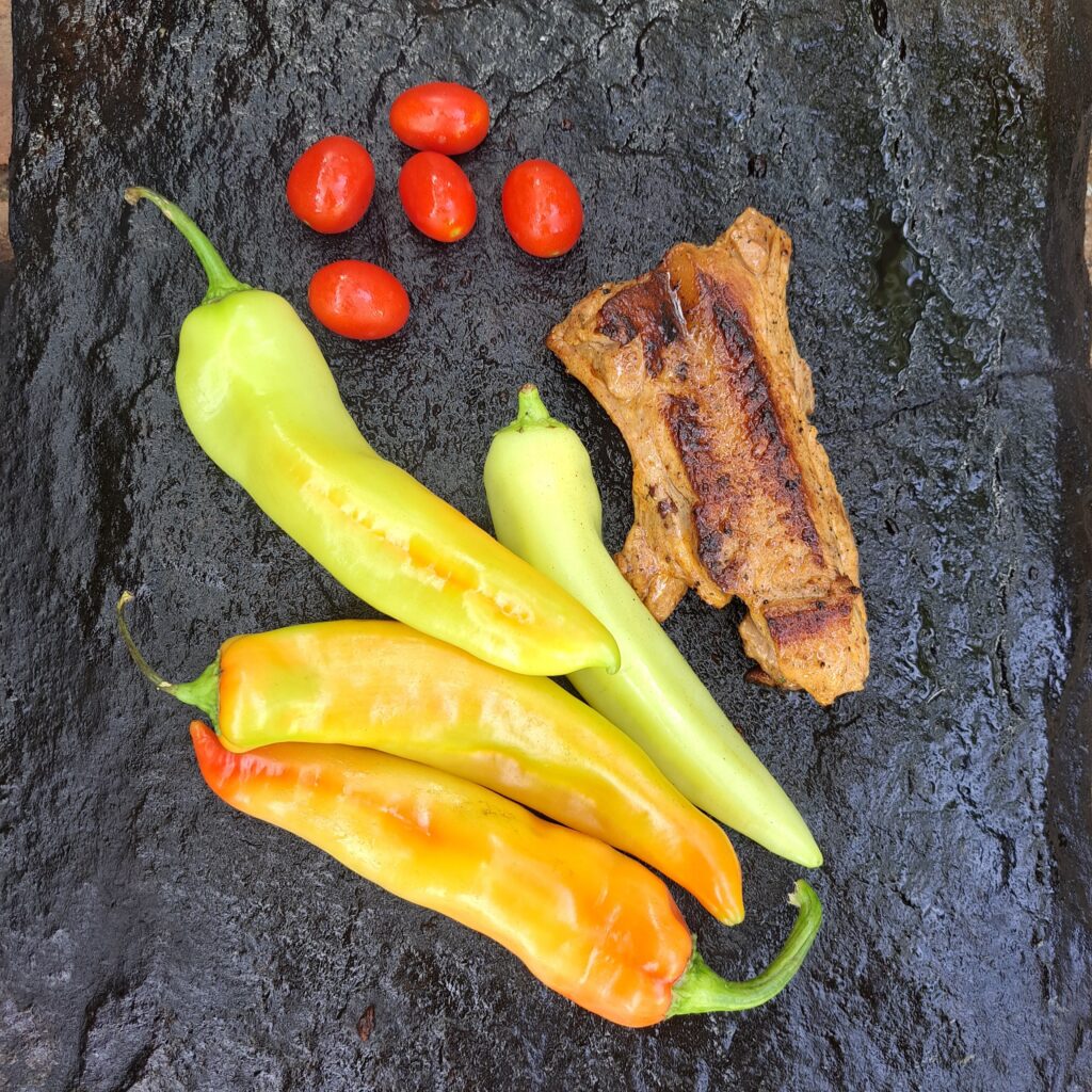 Whole peppers and cherry tomatoes grilling on a heated stone slab until nicely seared.