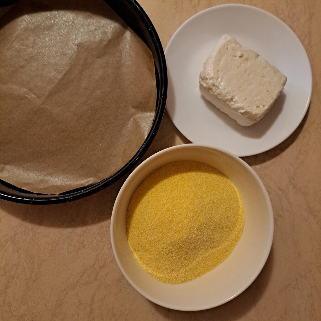 Ingredients for polenta rounds including a plate of polenta, a piece of goat cheese, and a baking tray with parchment paper.