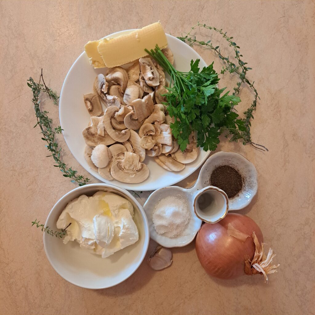 Chopped mushrooms, onion, garlic, butter, thyme, parsley, salt, pepper, and heavy cream arranged on a kitchen table.