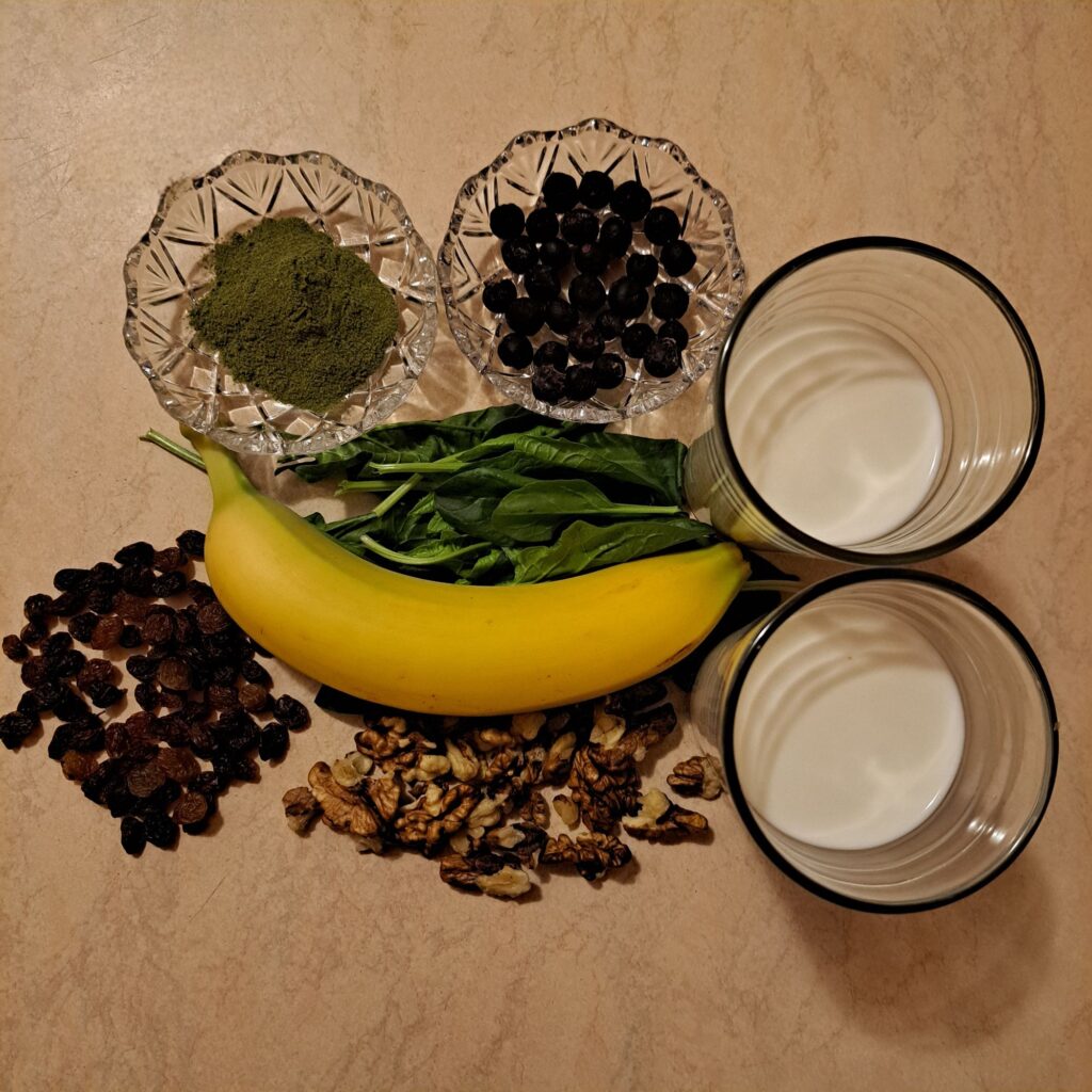 Moringa powder, spinach, banana, raisins, aronia berries, walnuts, milk, and yogurt arranged on a table.