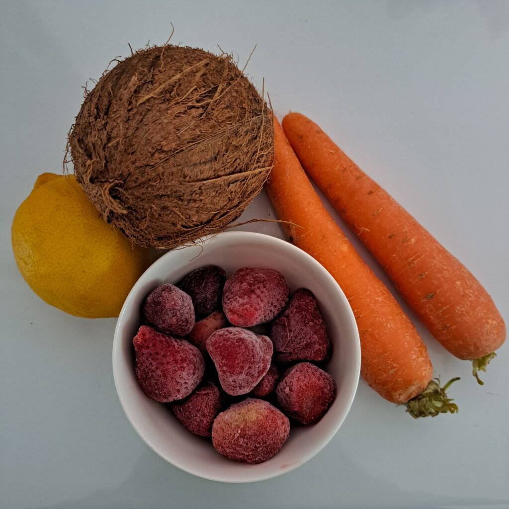 Carrots, strawberries, coconut, and lemon arranged on a table.