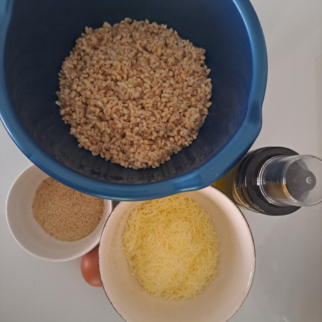 Cooked barley, breadcrumbs, grated parmesan, olive oil, and egg arranged neatly on a kitchen table.