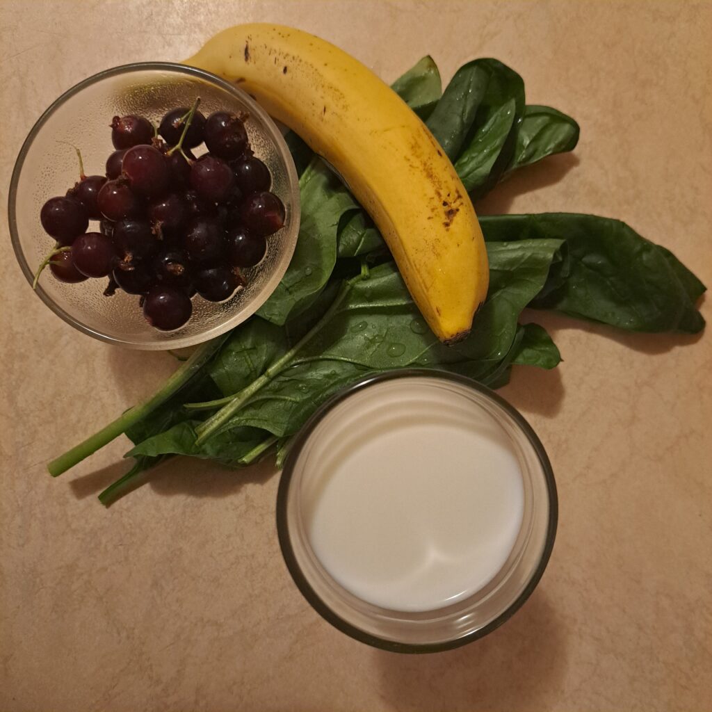 Fresh black currants, spinach, banana, and milk arranged on a table ready for blending.