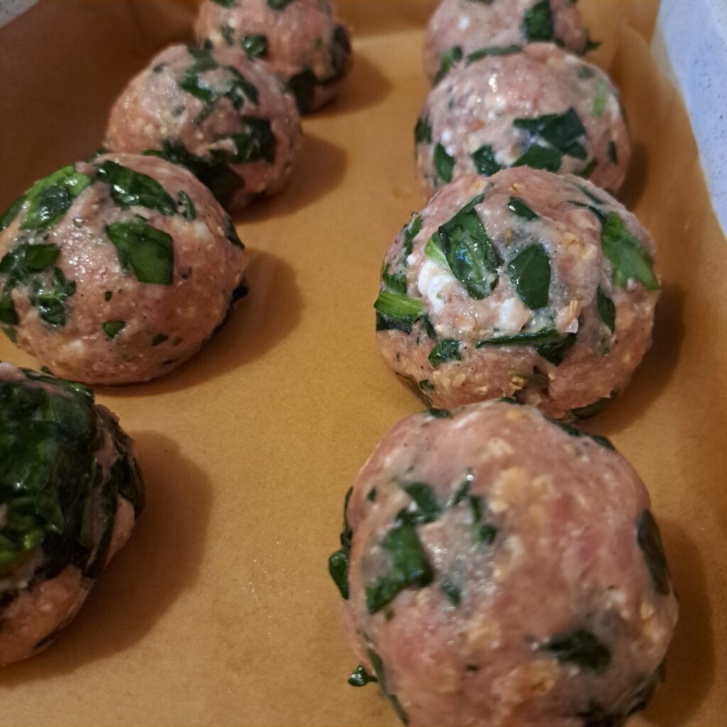 Unbaked turkey meatballs arranged on a baking tray lined with parchment paper, prepared for the oven.