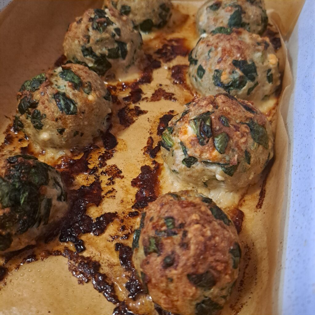 Golden baked turkey meatballs with spinach and feta on a baking tray, ready to serve.