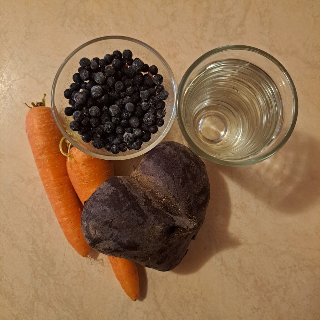 Whole beetroot, two carrots, fresh blueberries, and water ready for juicing.