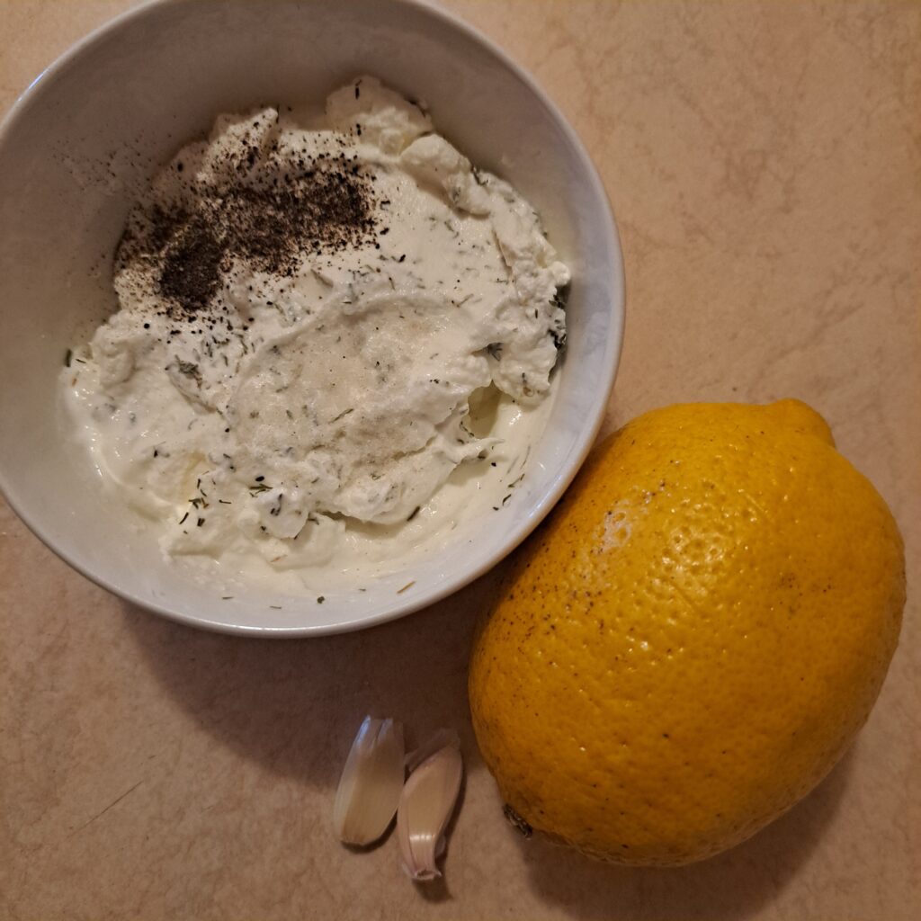 Yogurt mixed with dill, salt, and pepper, with garlic cloves and a whole lemon on the side.