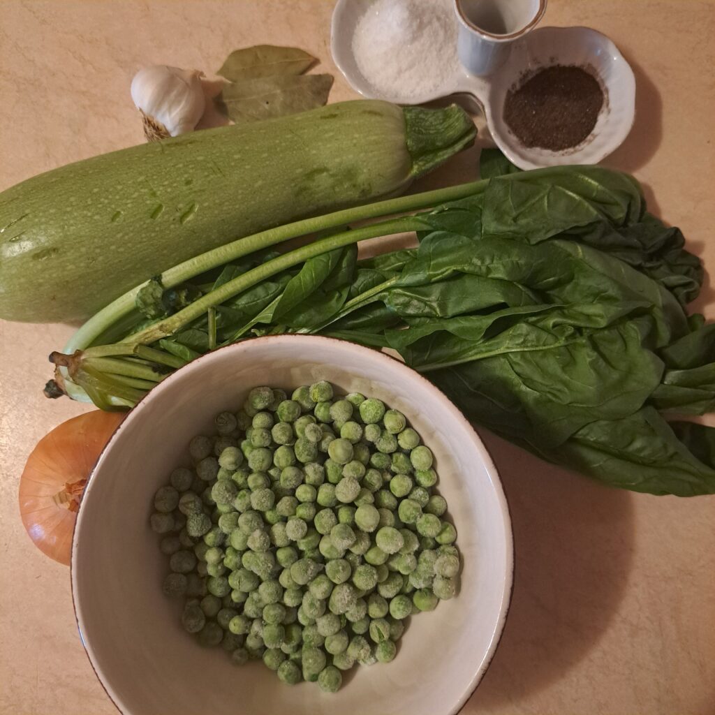 Peas, zucchini, spinach, onion, garlic, salt, black pepper, and a bay leaf arranged on a table.