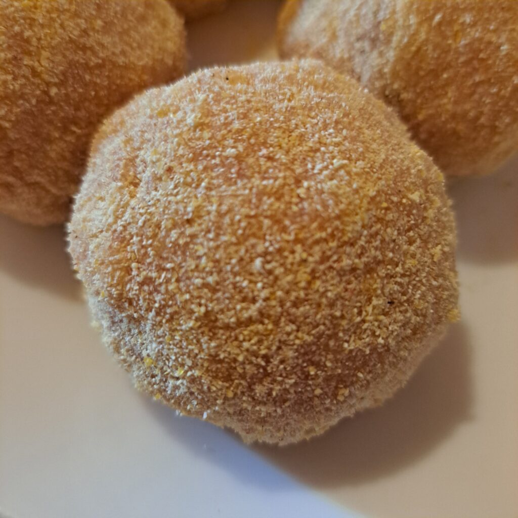 Unfried chicken balls shaped and rolled in cornmeal ready for cooking.