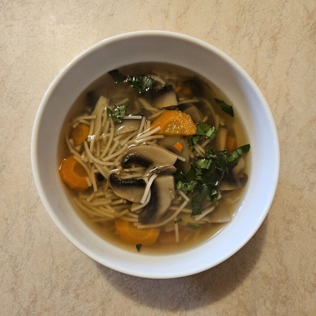 Served clear mushroom and vegetable soup in a bowl, garnished with fresh parsley.