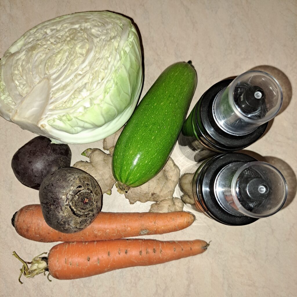 Fresh ingredients on a table for colorful vegetable salad including beetroot, carrot, cabbage, zucchini, sesame oil, ginger, and soy sauce.