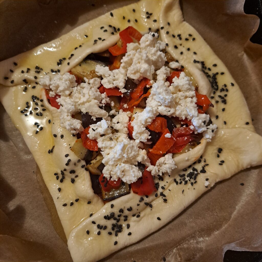 Rustic egg veggie galette on parchment paper in a baking tray, with folded edges and colorful roasted vegetables, ready for baking.