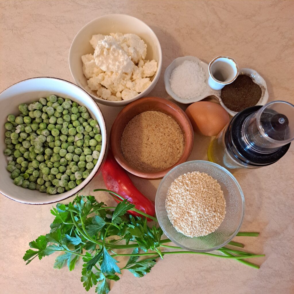 Ingredients arranged on the table for Pea Cheese Bites with Sesame – peas, cheese, red pepper, egg, breadcrumbs, sesame, parsley, salt, and black pepper.