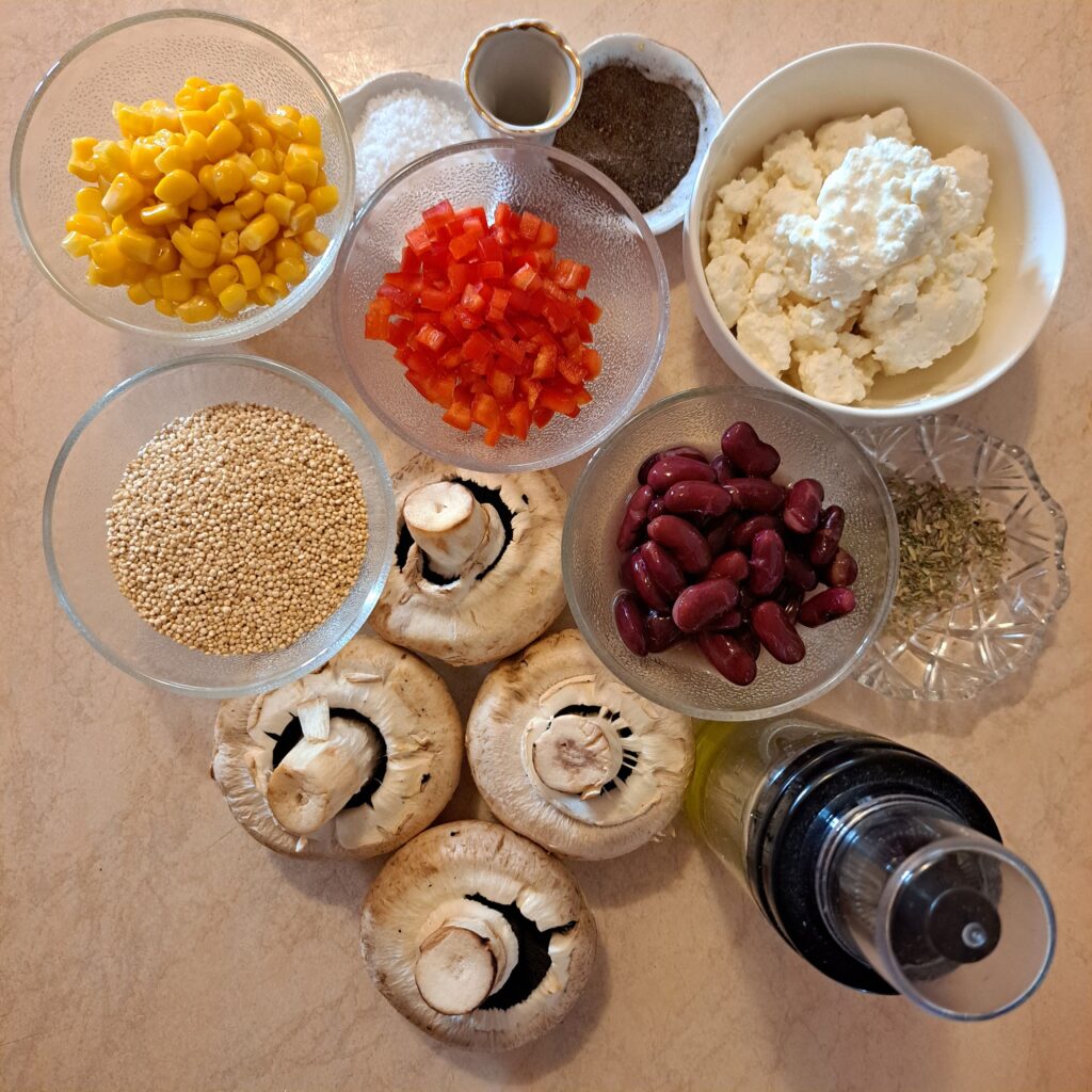 Ingredients arranged on a table for Quinoa Stuffed Mushrooms with Cheese – large mushrooms, quinoa, black beans, corn, chopped red pepper, cheese, oil, salt, and black pepper.