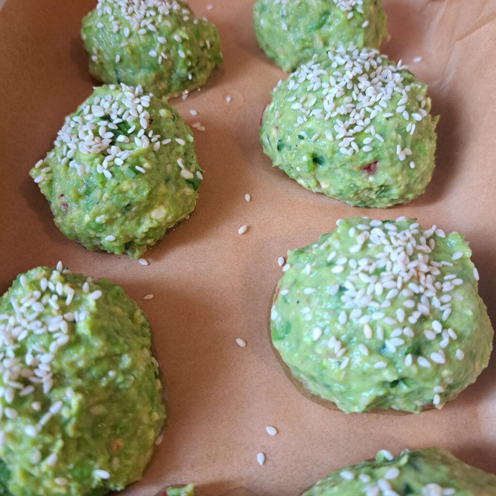 Unbaked Pea Cheese Bites with Sesame arranged on parchment paper in a baking tray ready for the oven.