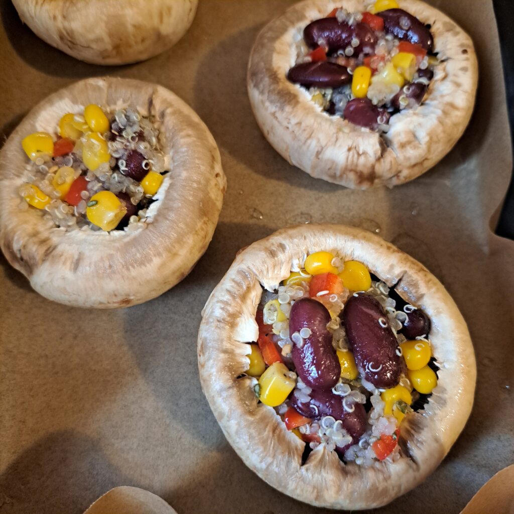 Mushrooms stuffed with quinoa, black beans, and corn arranged on parchment paper in a baking tray ready for baking.