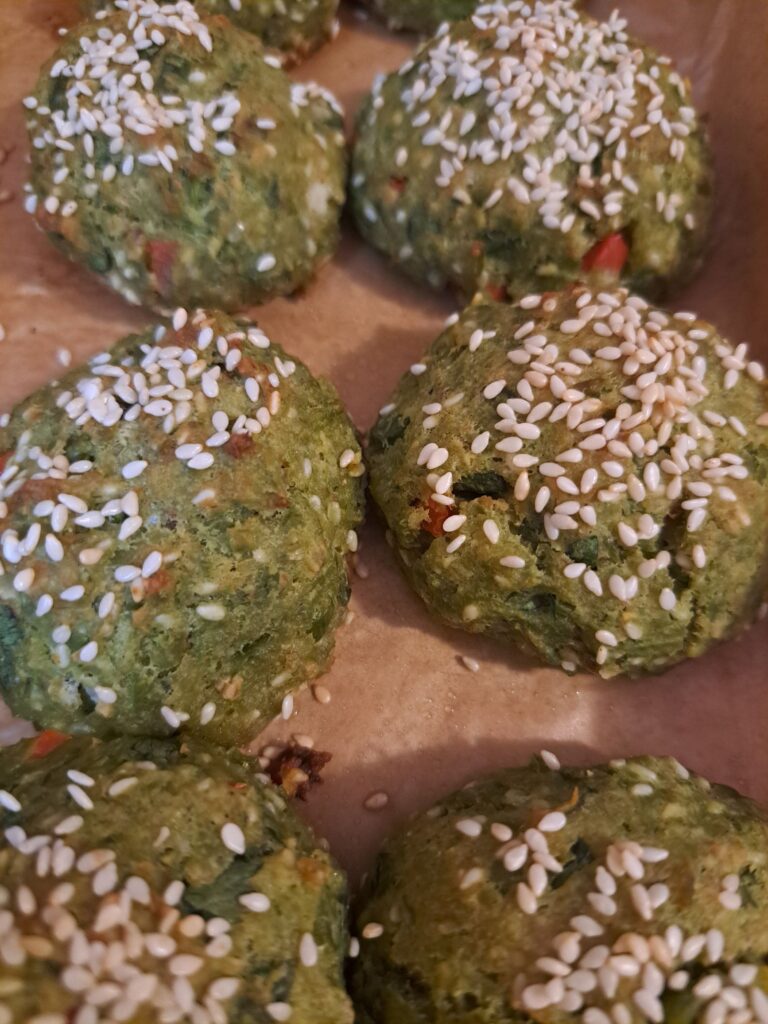 Freshly baked Pea Cheese Bites with Sesame on parchment paper in a baking tray.