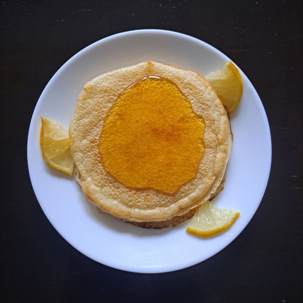 Unrolled mini crepes with ginger and lemon arranged on a plate, drizzled with honey, and decorated with lemon wedges, top view.