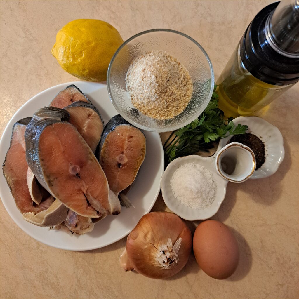 Ingredients for Salmon Cakes with Microgreens arranged on a table - salmon pieces, breadcrumbs, onion, garlic, parsley, egg, lemon, salt, and pepper.
