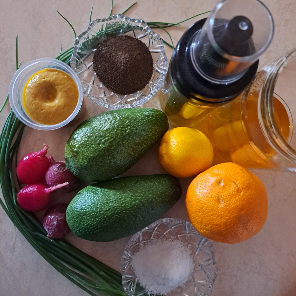 Two avocados, several whole radishes, orange, lemon, mustard, honey, fresh chives, salt and black pepper neatly arranged on table.