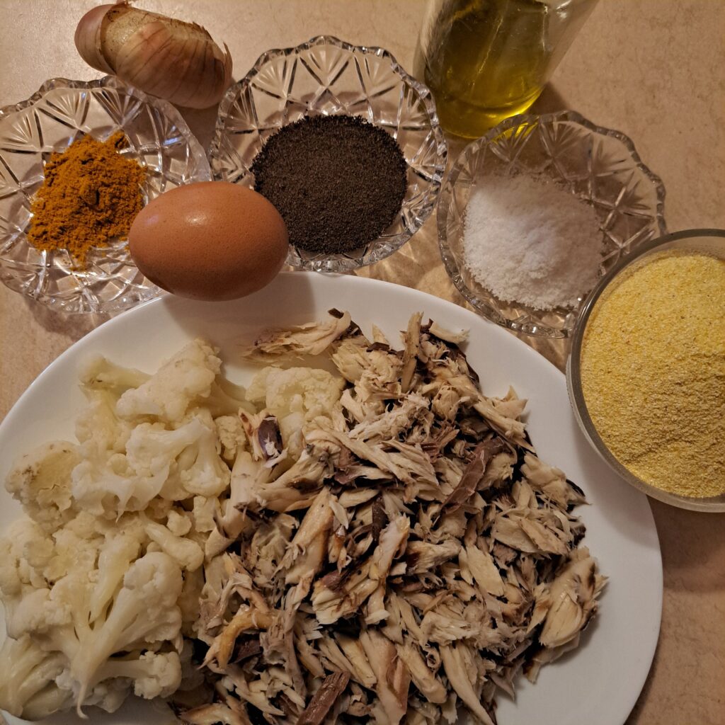 Chopped cooked mackerel, boiled cauliflower, cornmeal, egg, onion, olive oil, salt, black pepper, and turmeric arranged on a table.