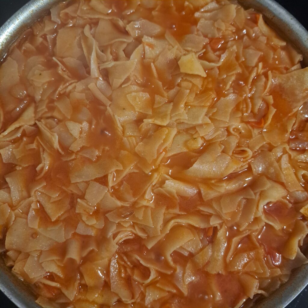 A close-up of Homemade Dried Pasta Delight in a pan, showing tender pasta sheets and colorful vegetables.