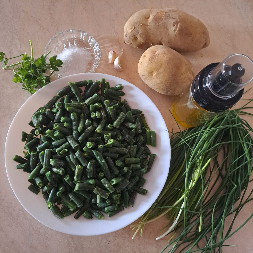 Ingredients for Boiled Potato Garden Plate: potatoes, green beans, fresh chives, parsley, garlic, olive oil, and salt arranged neatly on a kitchen table.