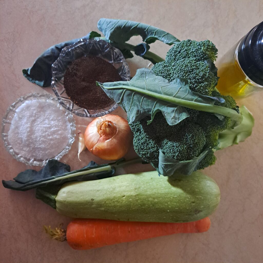 Fresh broccoli, carrot, zucchini, onion, garlic, olive oil, salt, and black pepper arranged on a kitchen table.