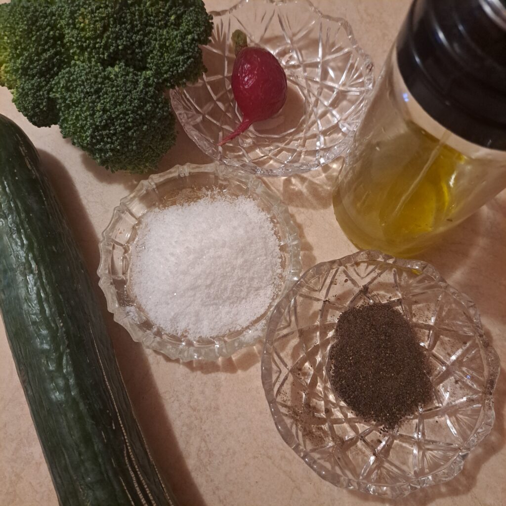 Fresh broccoli, cucumber, radish, salt, black pepper, and olive oil on kitchen table.