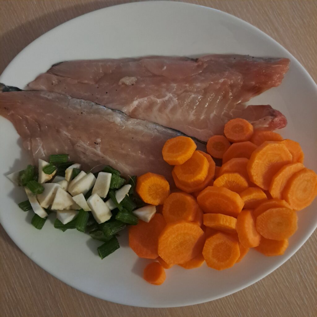 White fish fillets, sliced carrots, and celery arranged on a white plate. 