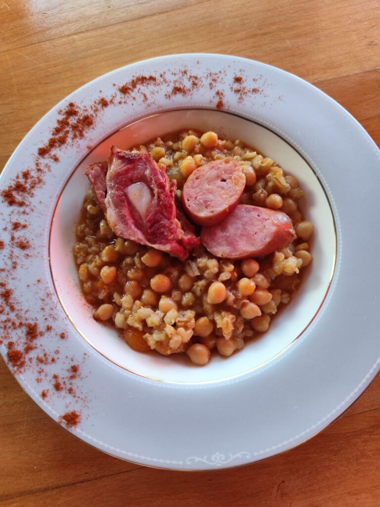 Served Barley Chickpea Meat Stew with smoked pork, sausages, chickpeas, and vegetables in a deep plate, ready to enjoy.