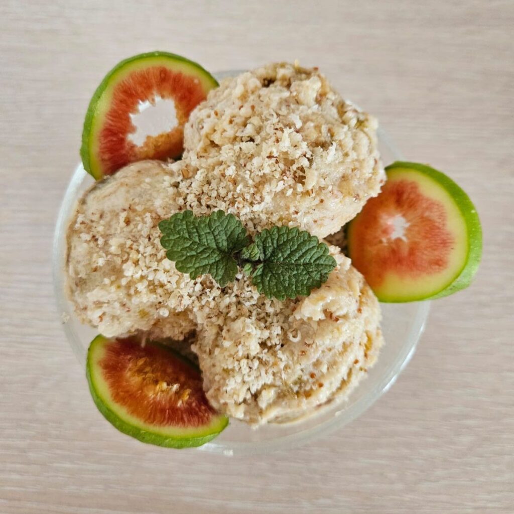 Three scoops of green fig ice cream with plenty of ground walnuts and decorated with fresh fig slices.