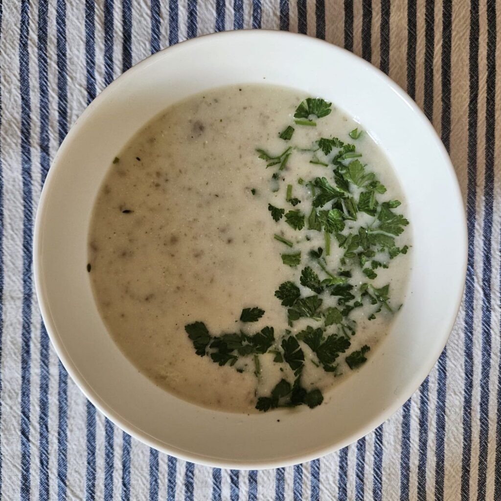 Finished creamy porcini mushroom soup in a white bowl, garnished with fresh chopped parsley.