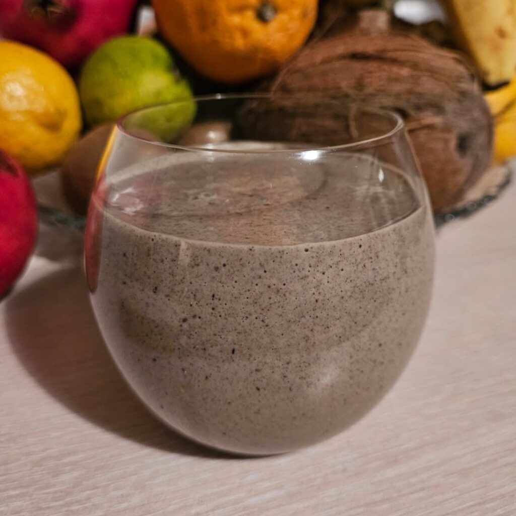 Smooth and creamy Moringa Walnuts Aronia Smoothie served in a glass with fruits in the background.