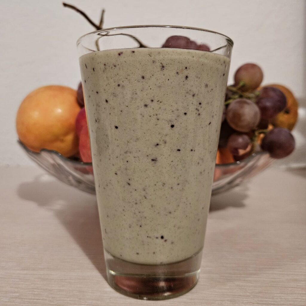 Smooth and creamy Berries Hazelnuts Spinach Smoothie served in a glass with fruits in the background.